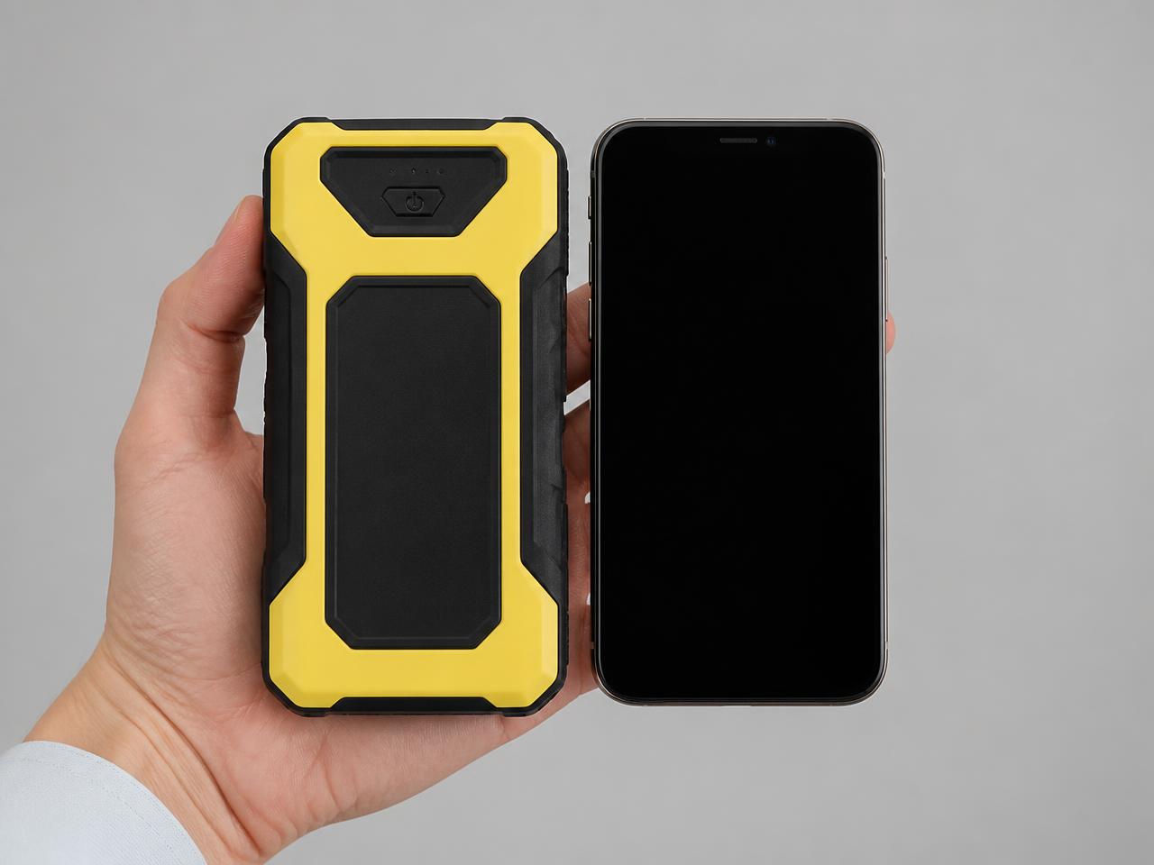The jump starter held in one hand next to a smartphone, showing it is roughly phone-sized